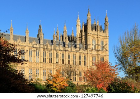 Houses of Parliament viewed through adjacent autumn-colored trees and bushes, London, UK.