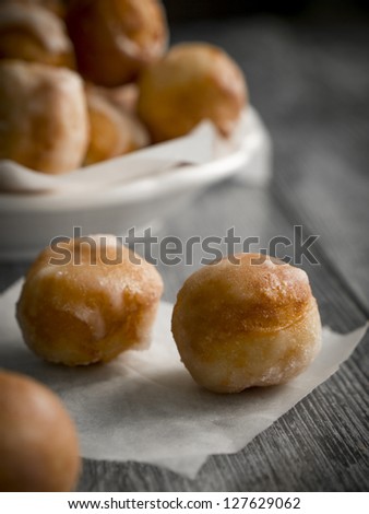 Small homemade doughnuts, also known as doughnut holes, prepared for Polish Fat Thursday. On the foreground three doughnuts on a piece of baking paper, in the background a white bowl full of doughnuts