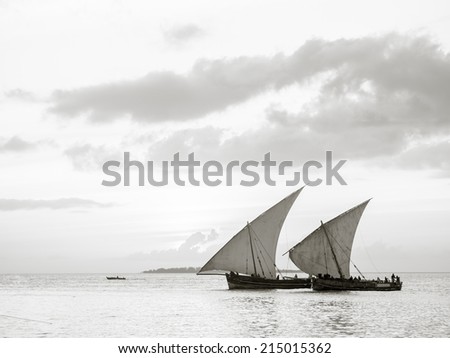 Horizontal black and white photo of two dhow boats on Indian Ocean close to Stone Town on Zanzibar, Tanzania in Africa, island at sunset.
