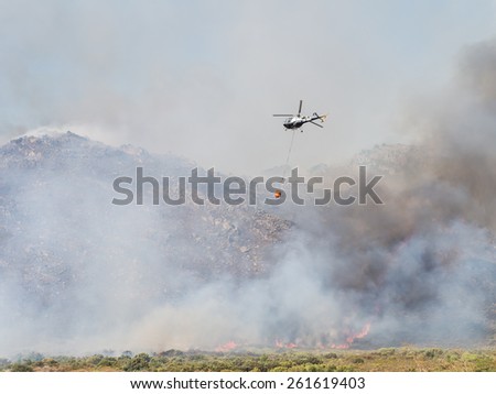 WESTERN CAPE, SOUTH AFRICA - FEBRUARY 17, 2015: Helicopter drops water over fire in Western Cape, South Africa, on a summer day. Fires are a common problem in Western Cape.