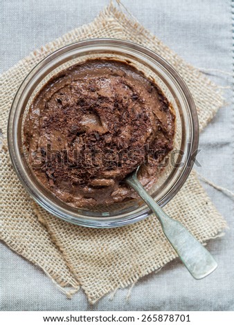 Vegan avocado chocolate mousse (pudding) in a glass bowl with a silver spoon inside. Rustic tablecloth in the background, close up. Vertical orientation, view from the above.