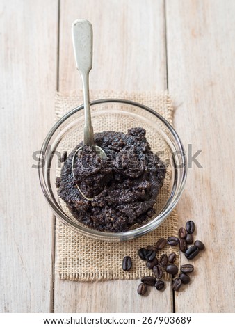 Homemade face and body organic all natural coffee scrub (peeling) with anti cellulite properties in a glass bowl, placed on a wooden table. Silver spoon inside. Vertical orientation.