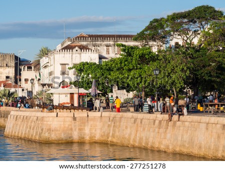 STONE TOWN, ZANZIBAR - MAY 02, 2015: Local people walking on the seafront in Stone Town, Zanzibar, Tanzania, East Africa and jumping to the water on the sunny evening. Horizontal orientation.
