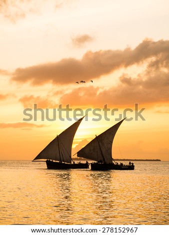 Colorful vertical photo of two traditional Tanzanian dhow boats on open sea on Indian Ocean close to Stone Town on Zanzibar island, Tanzania in East Africa, at orange sunset.
