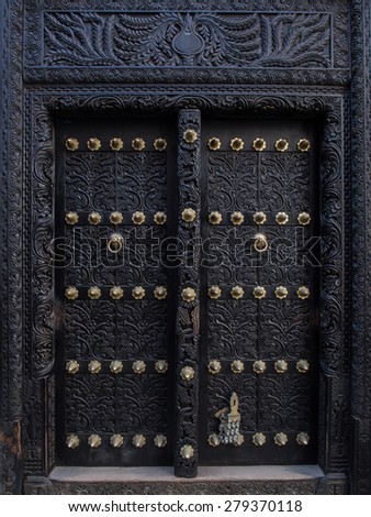 Vertical photo of old traditional black wooden carved door in Stone Town, Zanzibar, Tanzania, East Africa.
