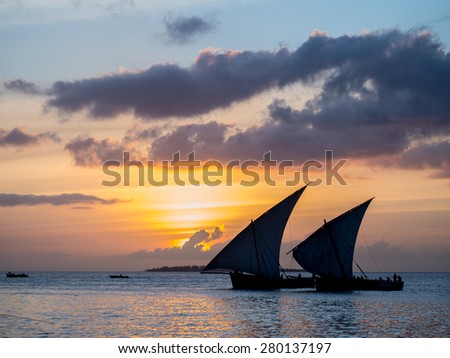 Colorful horizontal photo of silhouettes of two traditional Tanzanian dhow boats on open sea on Indian Ocean close to Stone Town on Zanzibar island, Tanzania in East Africa, at orange sunset.