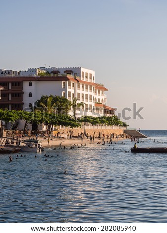 STONE TOWN, ZANZIBAR - MAY 02, 2015: Local people walking on the seafront in Stone Town, Zanzibar, Tanzania, East Africa and jumping to the water on the sunny evening. Vertical orientation.