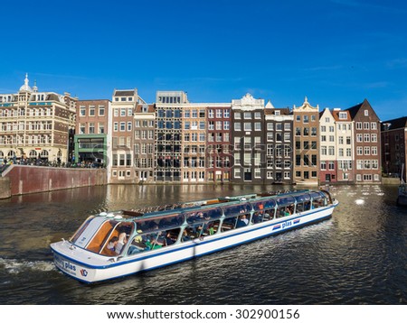 AMSTERDAM, NETHERLANDS - JUNE 15, 2015: Cruise tourist boat on a Damrak canal in Amsterdam, Netherlands, on a summer day. Traditional houses in the background.