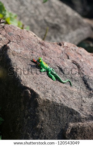 Installation with beautiful plasticine lizard clambering and having a rest on a stone in sunny weather