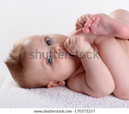 baby sucks toe lying on her back holding hands leg legs sucking his thumb on white background