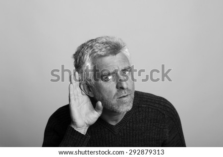 deaf aged older man listens with his hand to his ear in black and white