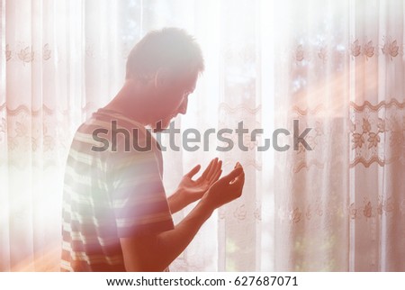 Young muslim man have a pray time with hands up in the air dua pose. Light beams comming from heaven bright window.