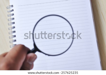 Hand Holding Magnifying Glass on Note Book, Focus on Note Book
