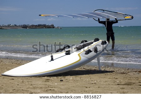 Male windsurfer carrying a sail into the water, surf board at the water edge close-up.