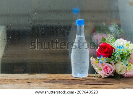 Cold water in bottle with flowers on wood table.beside glass window
