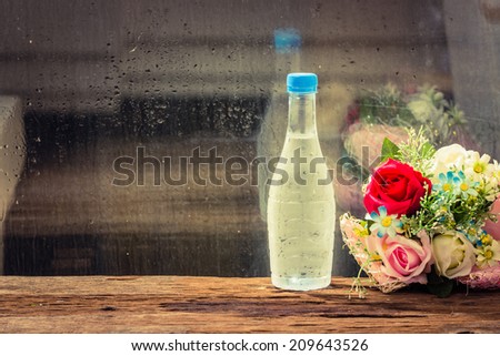 Cold water in bottle with flowers on wood table.beside glass window