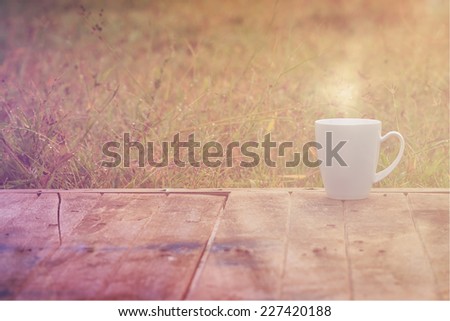 Steaming coffee cup on wood table. grass background