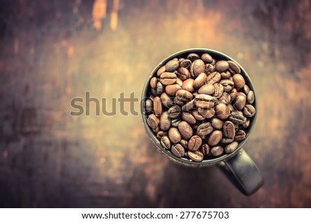 closeup of roasted coffee beans in cup on the wooden table, focus on coffee beans in cup