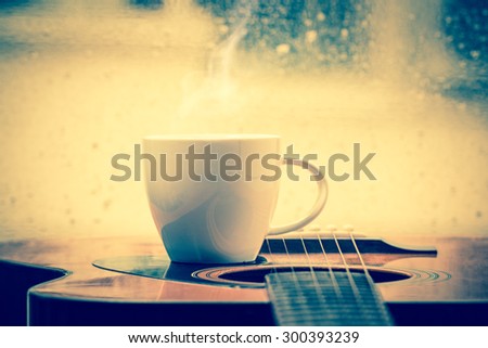 Coffee cup and acoustic guitar next the window with drop water