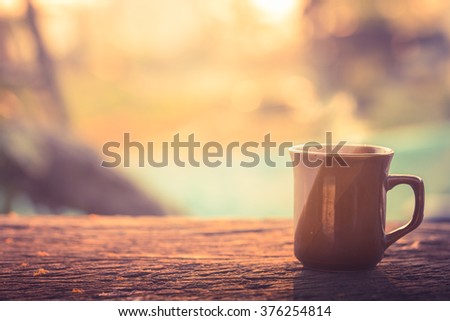 Coffee cup with hot coffee on old wood table in sunlight & blur green nature background