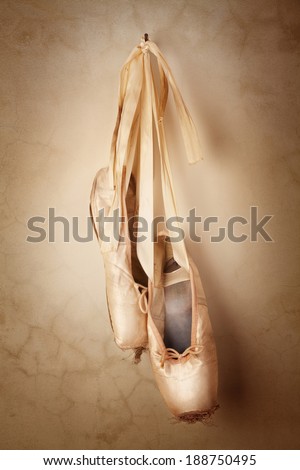 A well worn pair of pink ballet slippers hanging spotlit in front of a grunge wall.