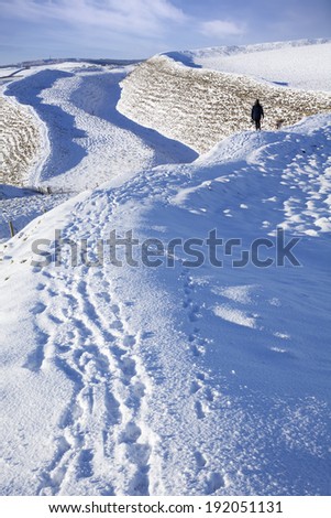 A solitary dog walker negotiates the snow on Maiden Castle, an iron age hillfort near Dorchester in Dorset, England