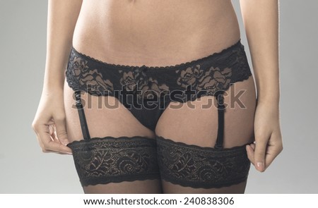 close up of beautiful sexy girl wearing black underwear with suspenders. hands on waist. isolated on gray studio background.