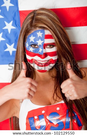 Happy American woman with the USA flag painted on her face with thumbs up