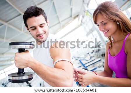 Gym man showing off muscles and woman measuring them