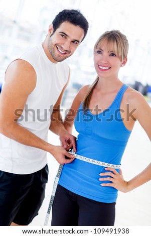 Personal trainer measuring a woman waist at the gym