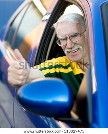 Happy senior man with thumbs up driving a car