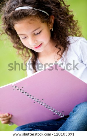 Little girl holding a notebook and studying at the park