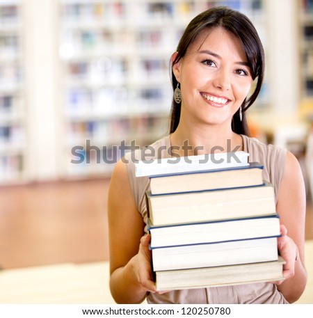 Female student carrying a pile of books at the library