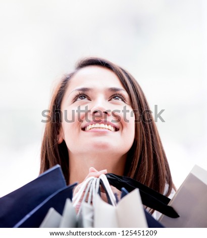Pensive female shopper looking up holding shopping bags