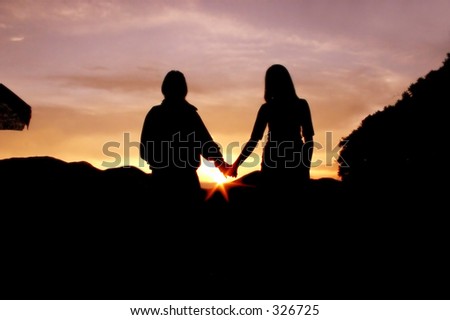 stock photo : couple of teenagers holding hands in front of a sunset in the 