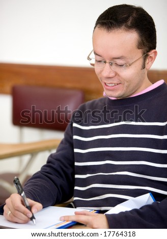 man studying in a classroom - smiling and writting on his notebook
