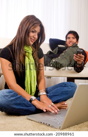 casual couple at home where she is on a laptop while he watches tv