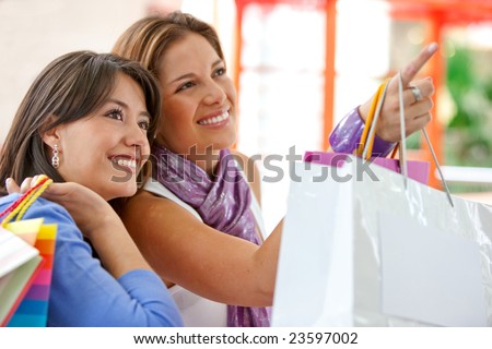 Shopping women with bags pointing out something on a shop window