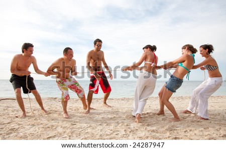 Group of friends competing pulling a rope at the beach - men against women