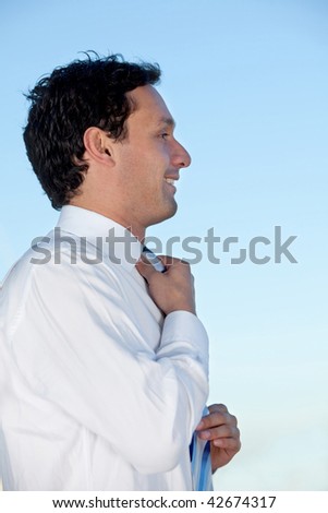 Handsome business man fixing his tie with a blue sky behind