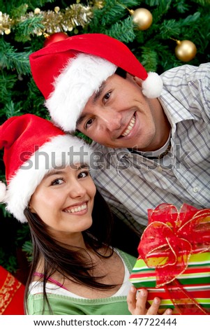 Christmas couple next to the tree with hats and a present
