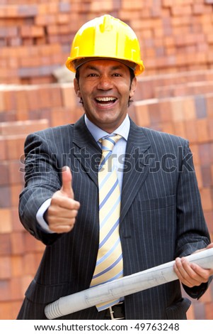 Happy engineer holding a model in a construction with his thumb up