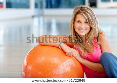 beautiful woman smiling and leaning on an orange pilates ball at the gym