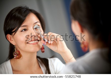 Woman looking in the mirror and curling her eyelashes - beauty concepts