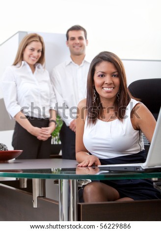 Business woman working on a laptop at the office and her team behind