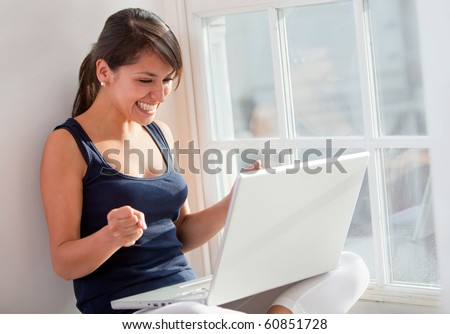 Woman sitting by a window with a laptop enjoying her online success