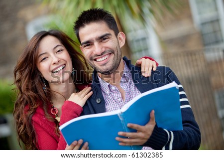 Happy couple of students with a notebook and smiling outdoors