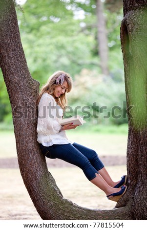 Beautiful woman sitting outdoors on a tree and reading a book