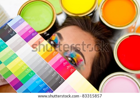 Female painter with a color palette covering her face and paint cans around her head