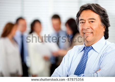 Business man smiling at the office with his team behind him
